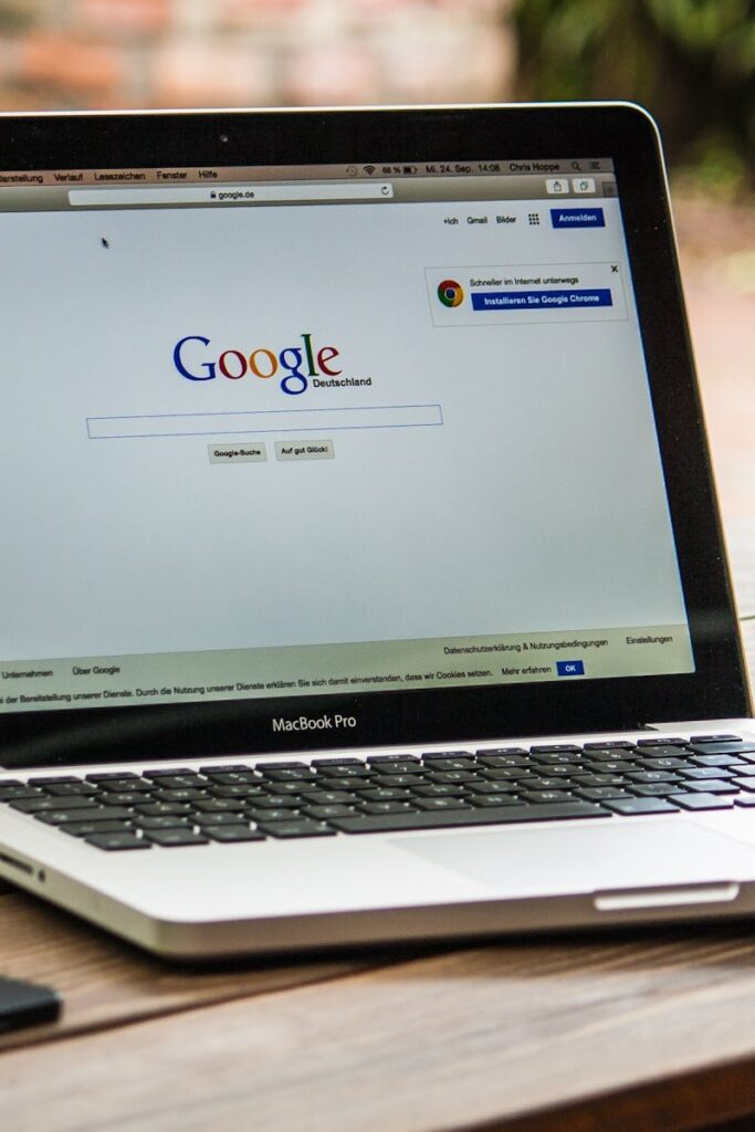 A MacBook Pro displaying Google Search on a wooden table outdoors, next to a smartphone.